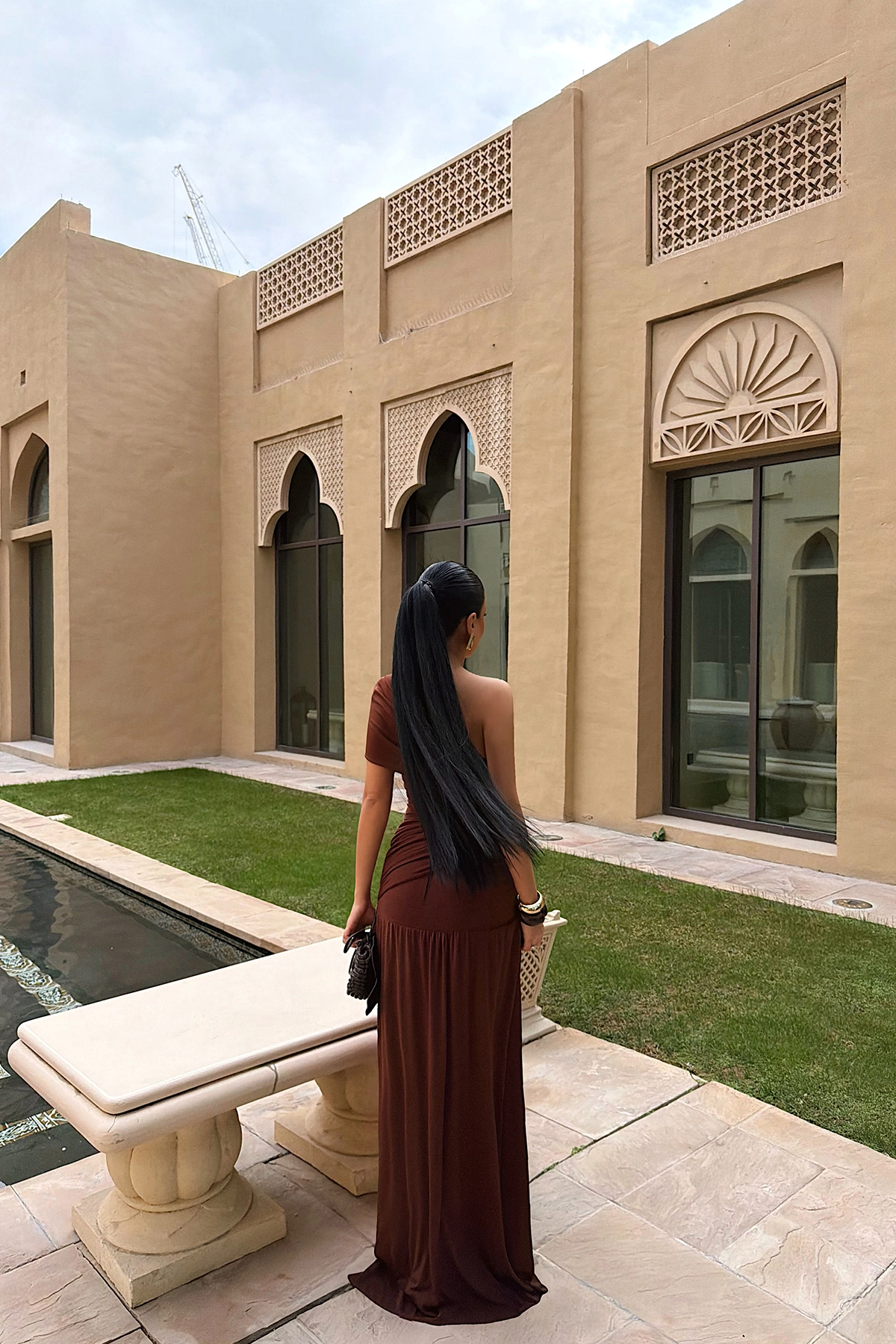 brown maxi dress featuring an elegant one-shoulder neckline, flattering ruched detailing and a softly draped skirt. Its refined silhouette creates an effortlessly glamorous look, perfect for evening events, weddings and special occasions.